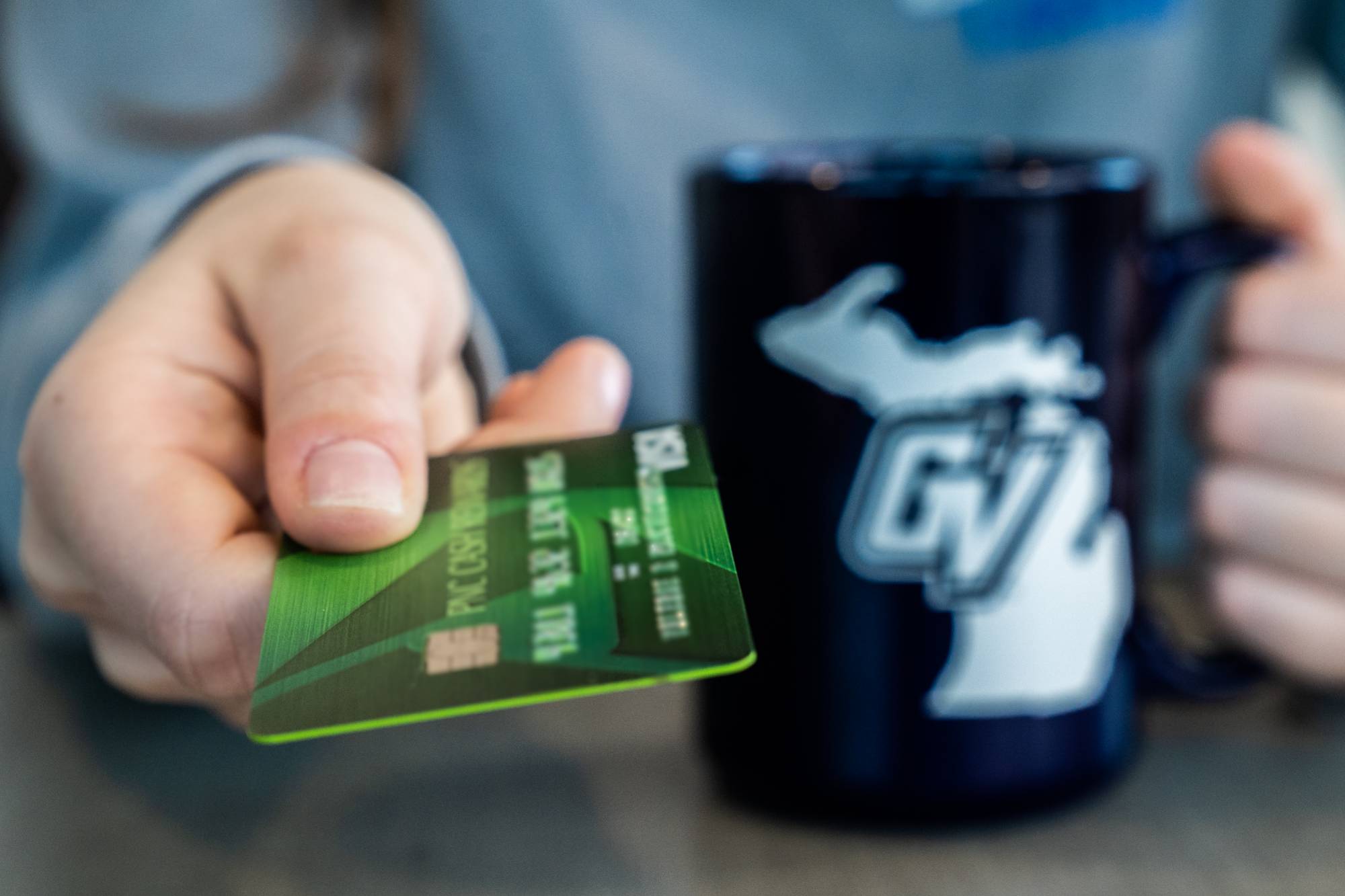 Hand presenting credit card while other hand is holding a GVSU coffee mug
